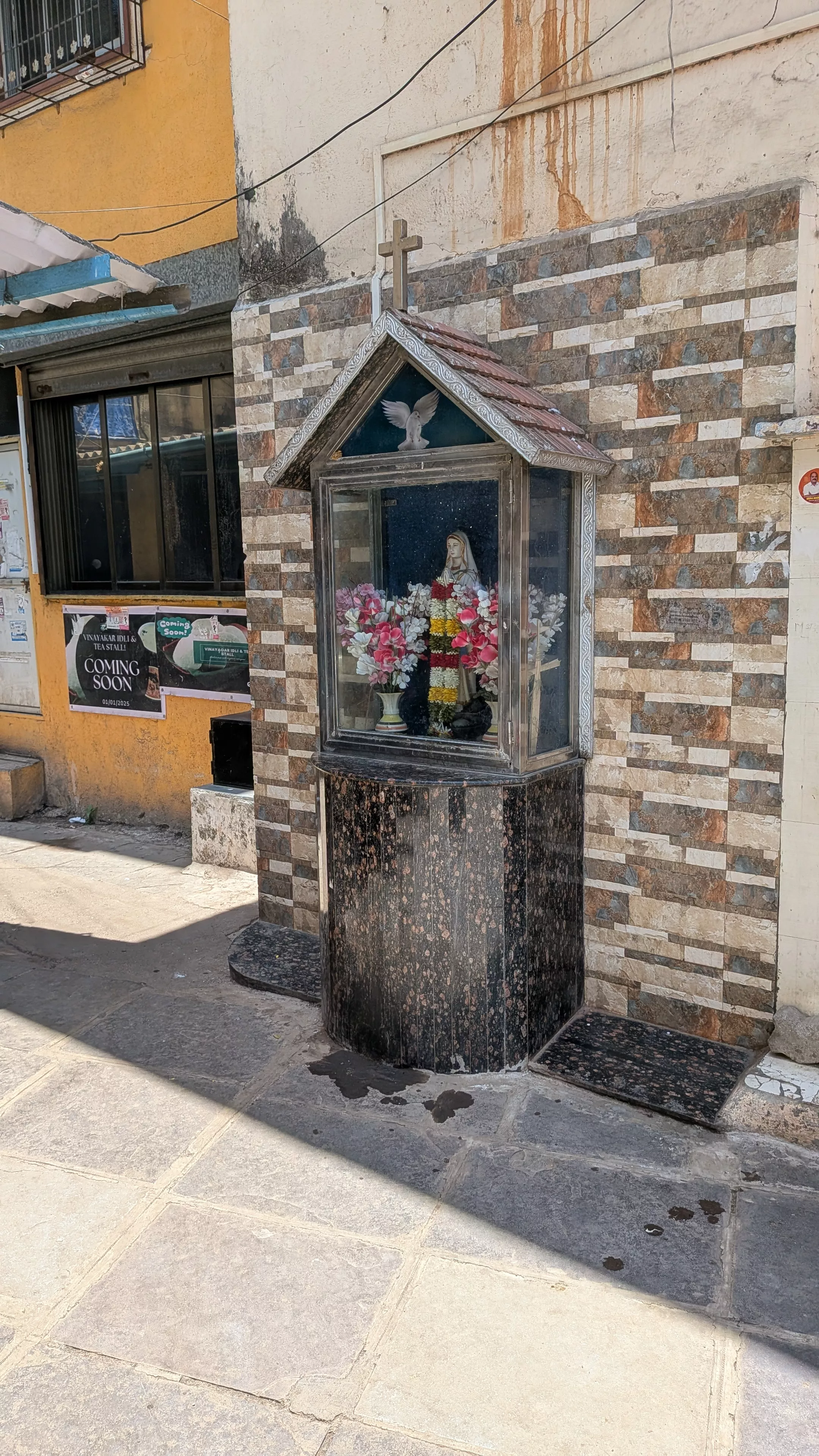A small shrine housing a statue of Mother Mary attached to the exterior of the building.