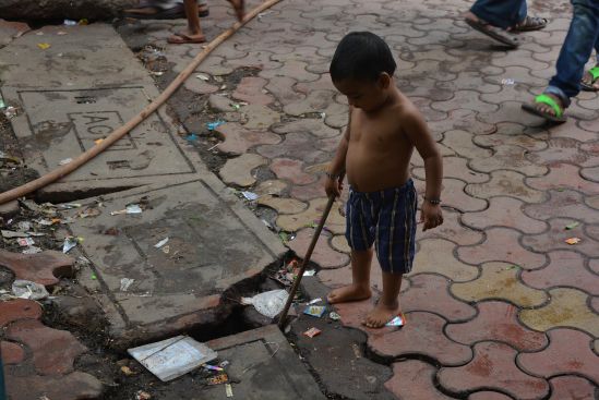 A kid playing with a stick in the gutter at Bareilly Compound.